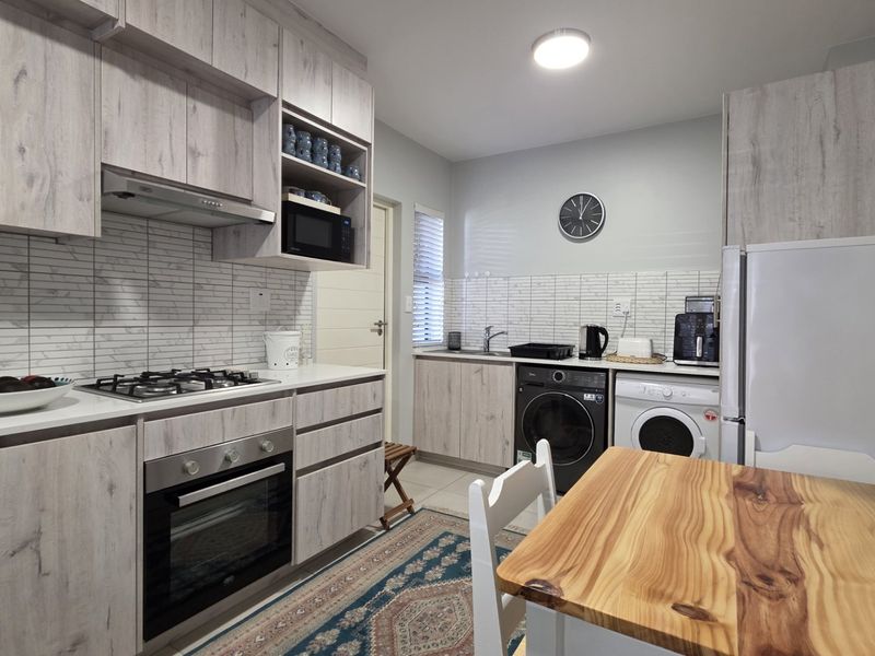 Modern kitchen featuring light wood-grain cabinetry, gas hob, built-in oven, and integrated laundry facilities with a clean tiled backsplash.