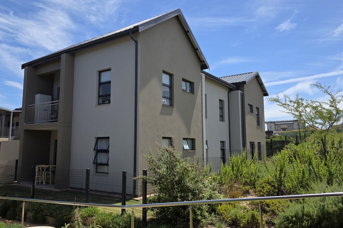 A view of the rear elevation of a modern apartment building featuring a metal roof, aluminium windows, and a private balcony.