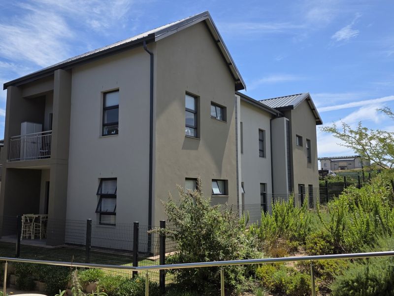 A view of the rear elevation of a modern apartment building featuring a metal roof, aluminium windows, and a private balcony.