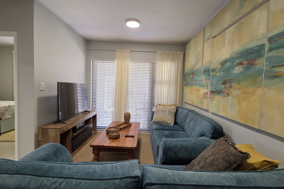 A comfortable living room featuring neutral walls, a sliding glass door with venetian blinds, and a view into the adjacent bedroom.