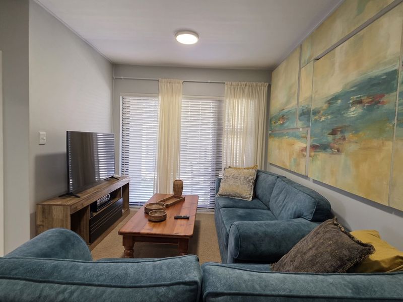 A comfortable living room featuring neutral walls, a sliding glass door with venetian blinds, and a view into the adjacent bedroom.