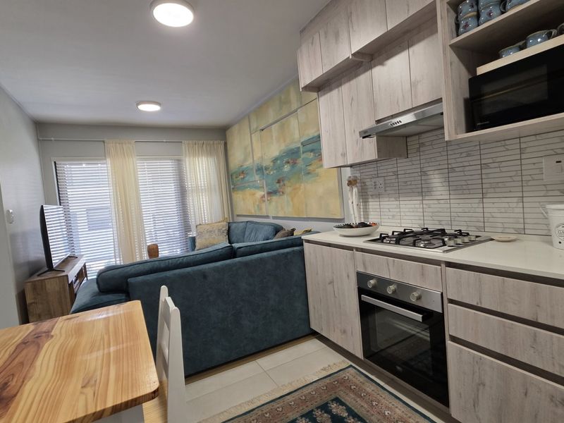 Modern open-plan living area featuring a well-equipped kitchen with light wood-grain cabinetry, gas hob, and integrated appliances, seamlessly flowing into the lounge space.