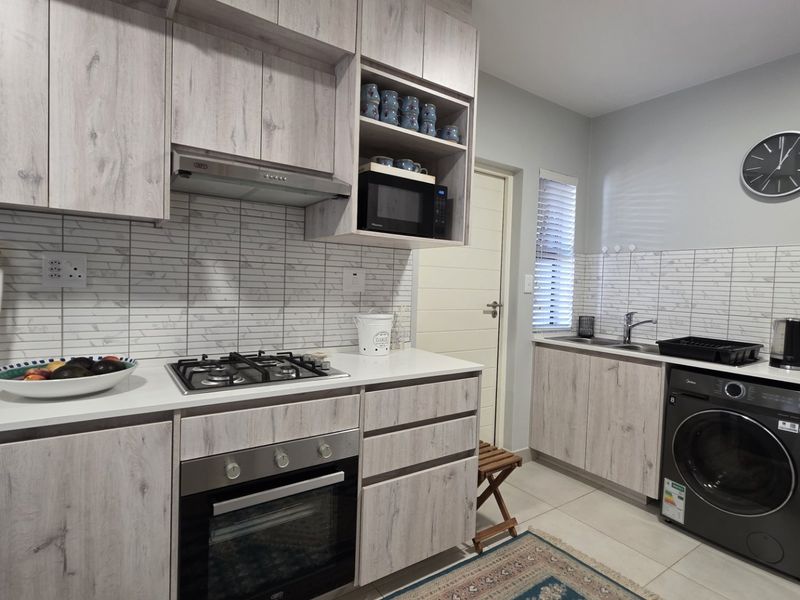 Modern kitchen featuring light wood-grain cabinetry, gas hob, built-in oven, extractor fan, and integrated laundry appliances with a clean tiled backsplash.
