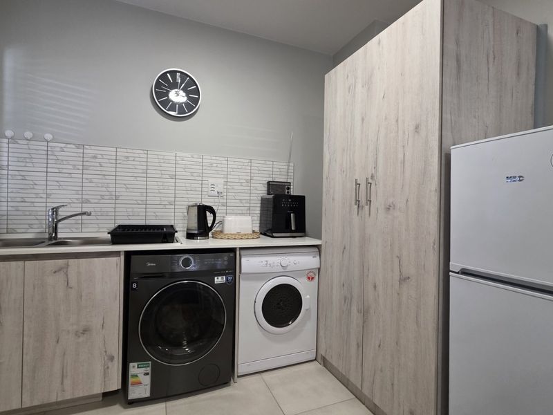 A functional laundry area featuring modern wood-look cabinetry, a stainless steel sink, tiled backsplash, and dedicated space for laundry appliances.