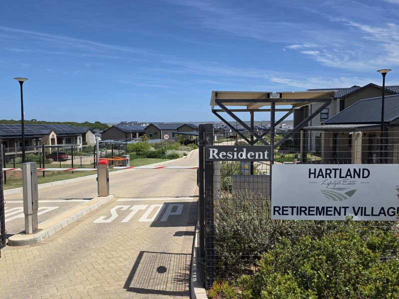Entrance view of Hartland Lifestyle Estate retirement village featuring a secure boom gate access point, paved driveway, and modern residential units.