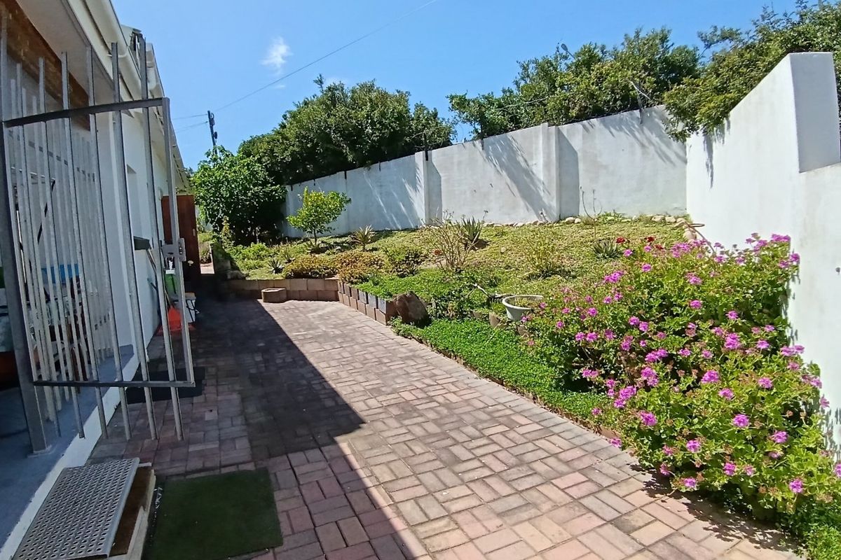 A well-maintained rear garden area featuring a paved walkway, landscaped terraced garden beds, and secure perimeter walling.
