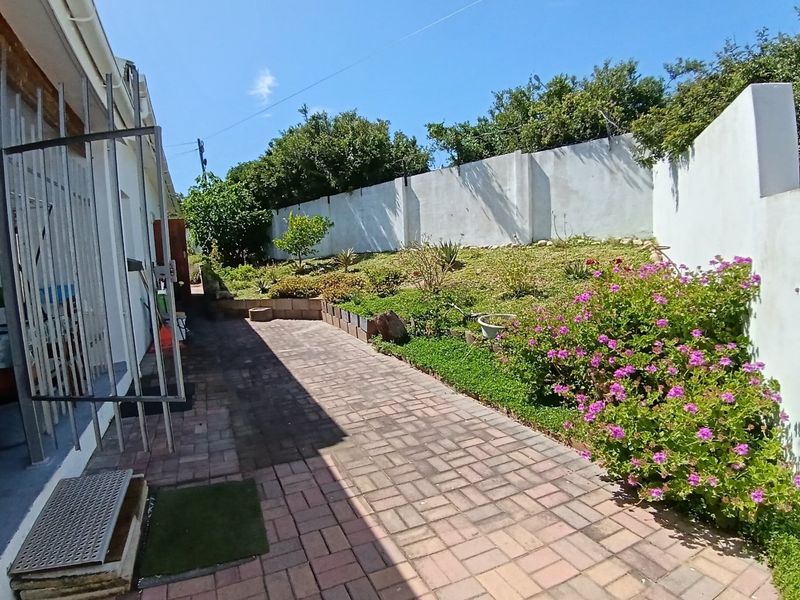 A well-maintained rear garden area featuring a paved walkway, landscaped terraced garden beds, and secure perimeter walling.