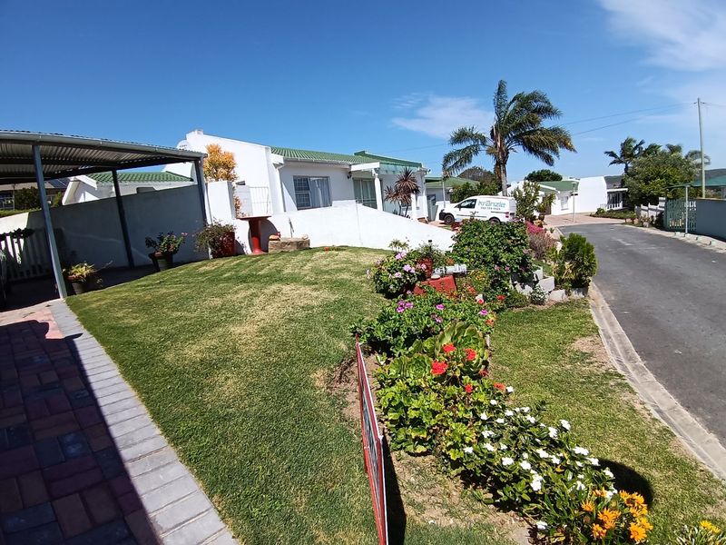 Front exterior view of the property featuring a well-maintained lawn, landscaped garden beds, a paved driveway, and a covered carport area.