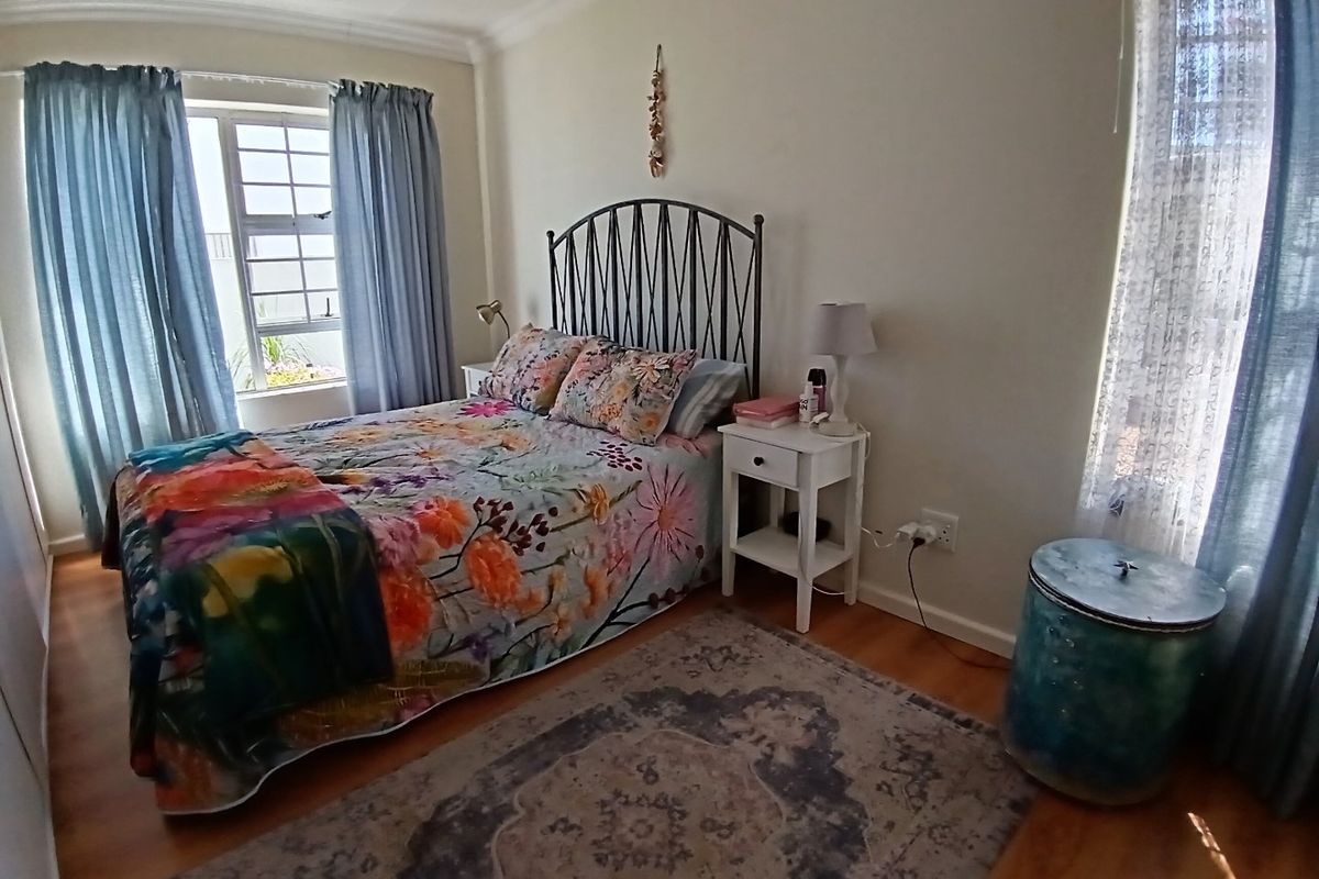 A cozy bedroom featuring laminate flooring, decorative cornicing, and dual windows that provide natural light.