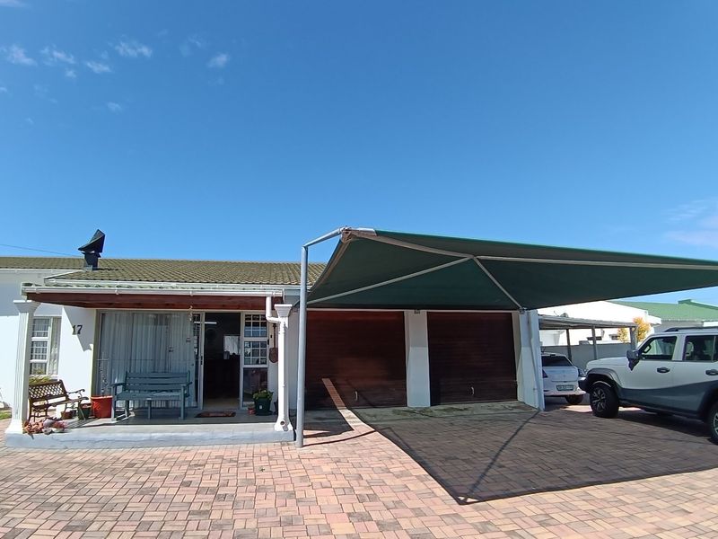 Front elevation of a residential property featuring a double garage, paved driveway, shade cloth carport, and a covered entrance porch.