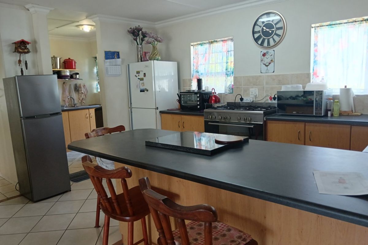 Functional kitchen featuring a central island, laminate cabinetry, gas stove, and tiled backsplash, with an adjoining scullery area.