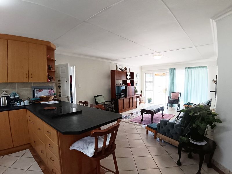 Open-plan living area featuring a functional kitchen with built-in cabinetry and tiled flooring, flowing into a bright lounge space with sliding door access.