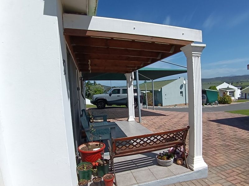 A covered outdoor patio area featuring tiled flooring, a timber pergola structure, and decorative columns, overlooking a paved driveway and residential surroundings.