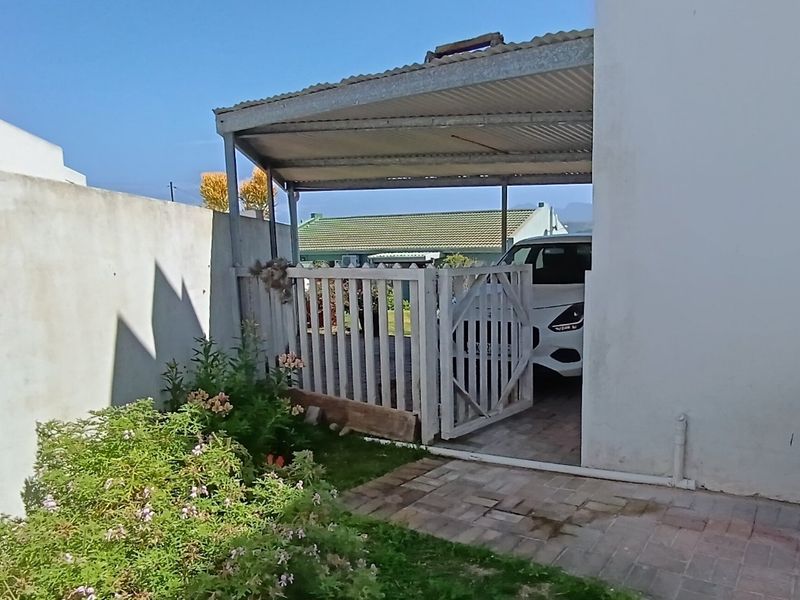 A covered carport area with a timber gate, paved driveway, and adjacent garden space.