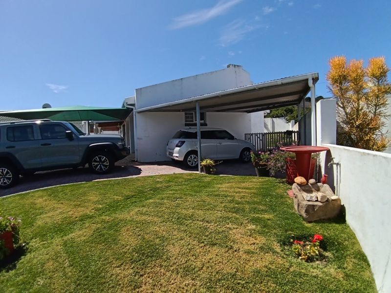 Front exterior view featuring a paved driveway, a covered carport, and a small garden area with boundary walling.