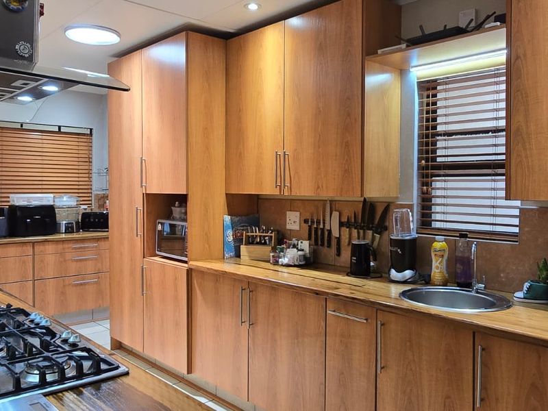 A well-maintained kitchen featuring warm wooden cabinetry, matching wooden countertops, a gas hob with extractor, and integrated stainless steel sink.