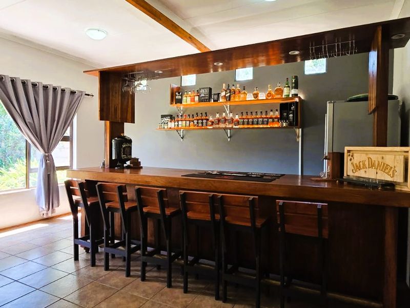 A well-appointed indoor bar area featuring a custom wooden counter, overhead canopy, built-in shelving, and tiled flooring, creating a dedicated space for entertainment.