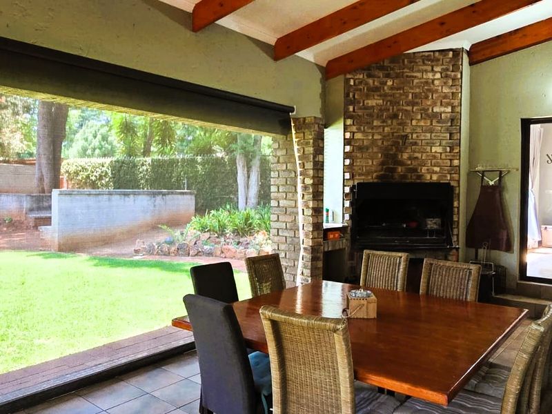 Covered patio featuring a built-in braai, exposed timber beams, and tiled flooring, offering seamless indoor-outdoor flow to the garden.