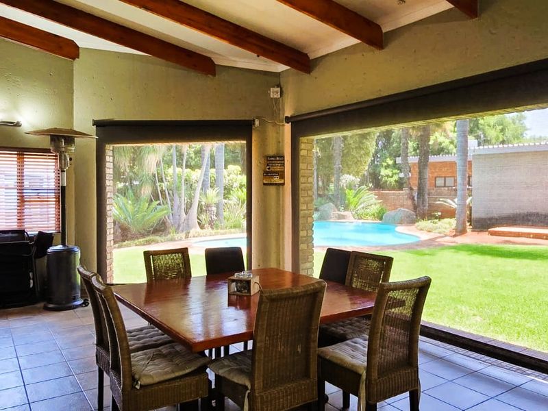 Spacious covered patio featuring exposed timber beams, tiled flooring, and a built-in bar, offering seamless indoor-outdoor flow to the garden and pool area.