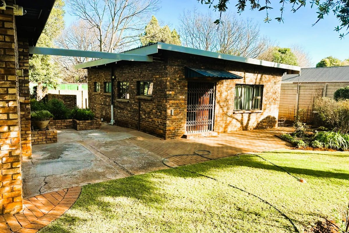 Rear view of a face brick outbuilding featuring a paved patio area, security gate, and established garden space.