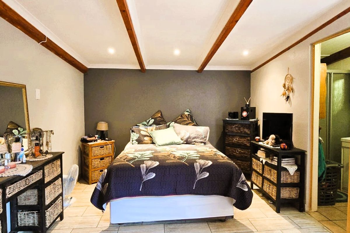 A bedroom featuring exposed timber ceiling beams, recessed lighting, and tiled flooring, with an adjoining en-suite bathroom.