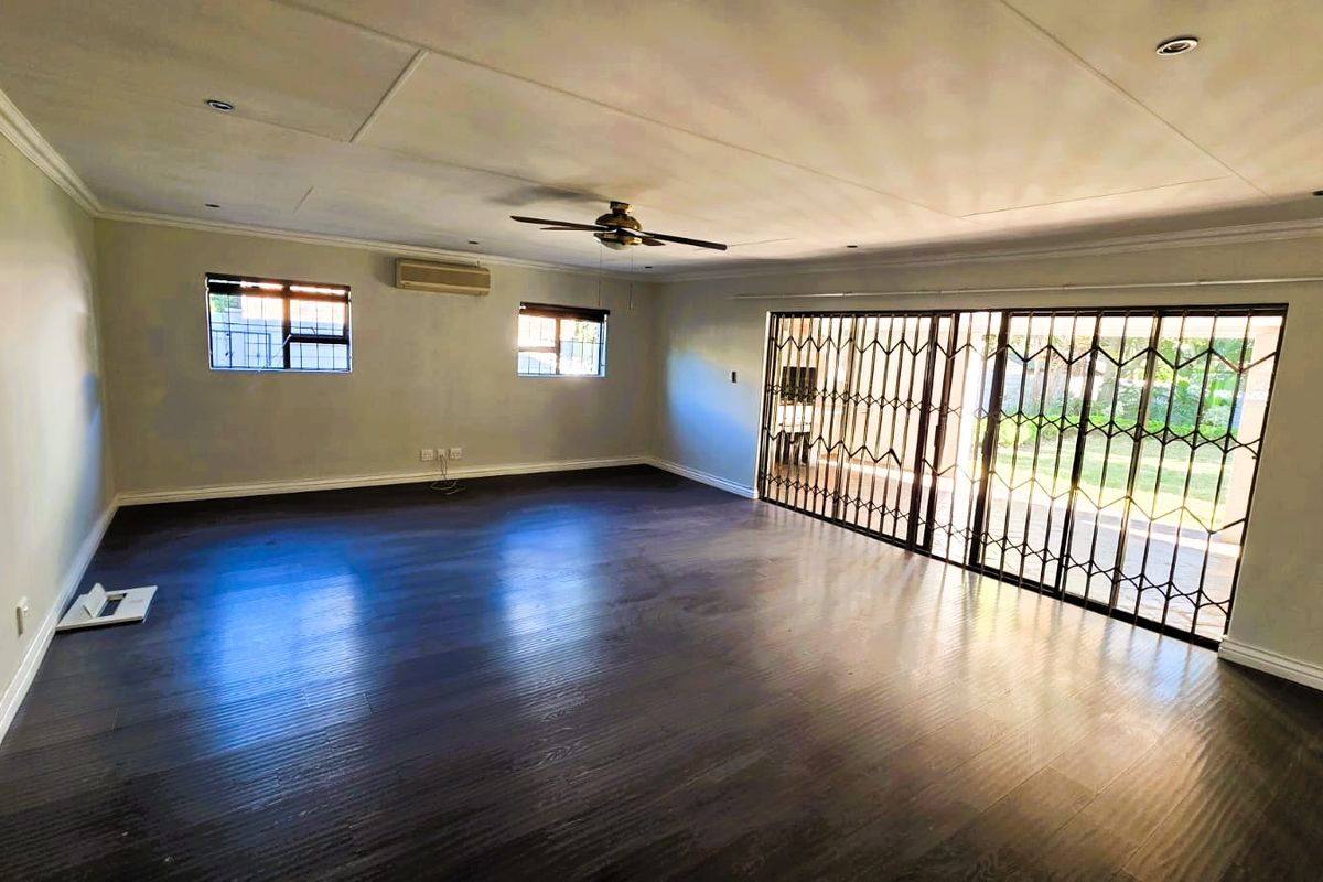 Spacious, empty living area featuring dark laminate flooring, a ceiling fan, split-system air conditioning, and large sliding doors with security gates leading outdoors.