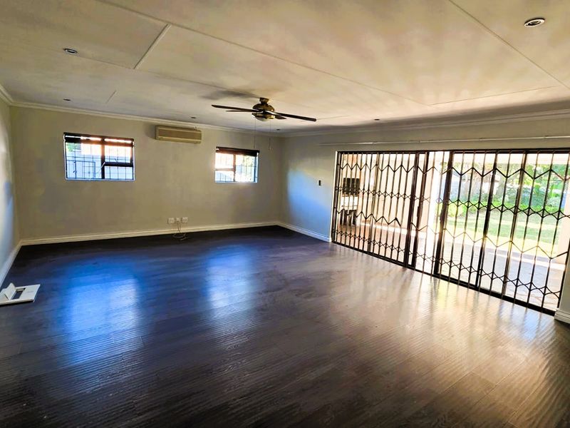 Spacious, empty living area featuring dark laminate flooring, a ceiling fan, split-system air conditioning, and large sliding doors with security gates leading outdoors.
