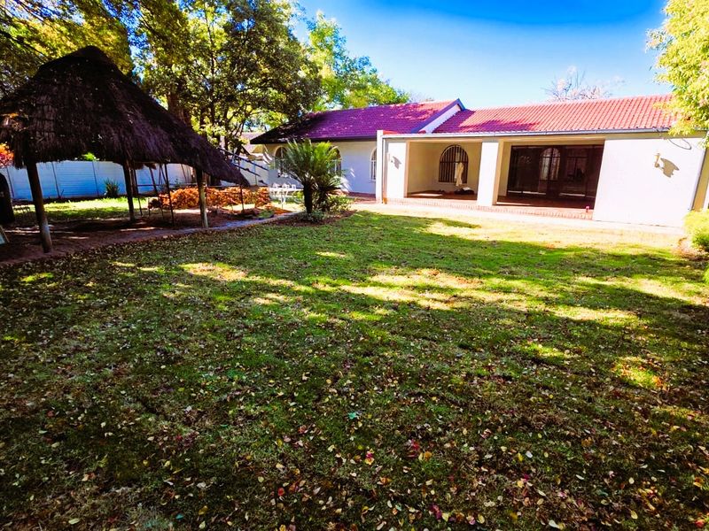Spacious rear garden featuring a large lawn, a traditional thatched lapa, and a covered patio area attached to the main house.