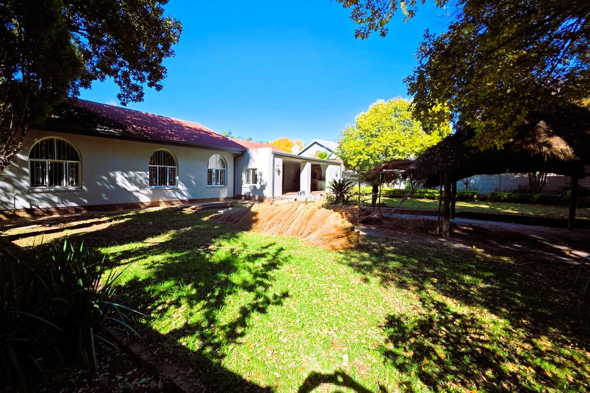 Rear view of the property featuring a spacious garden, a thatched lapa, and a covered patio area attached to the main house.