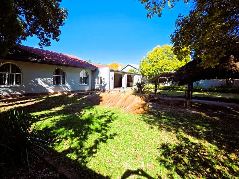 Rear view of the property featuring a spacious garden, a thatched lapa, and a covered patio area attached to the main house.