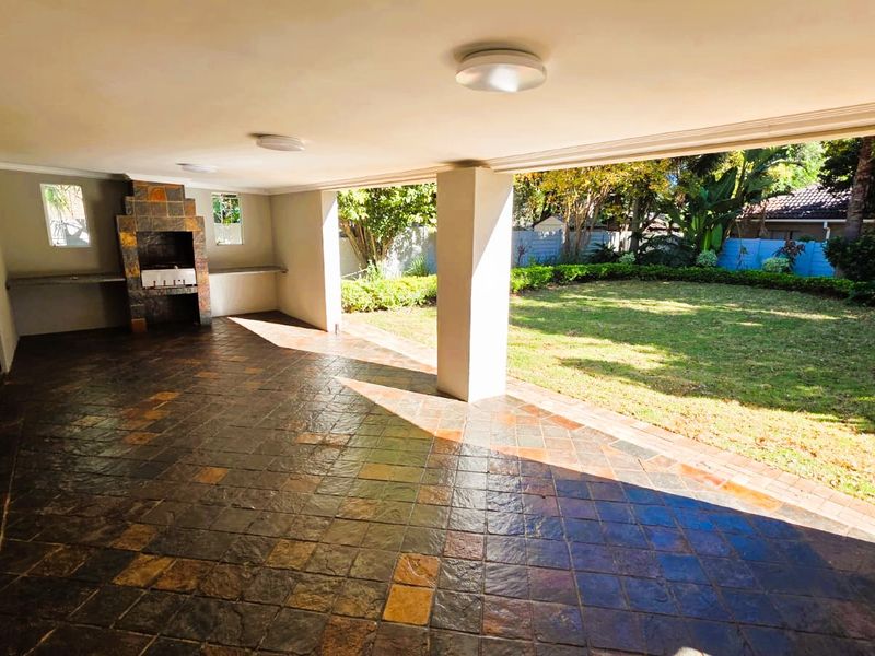 Spacious covered patio featuring slate tile flooring and a built-in braai, overlooking a private garden area.