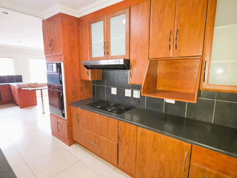 A functional kitchen featuring warm-toned wooden cabinetry, black stone countertops, a built-in oven, and an electric hob with an extractor fan.