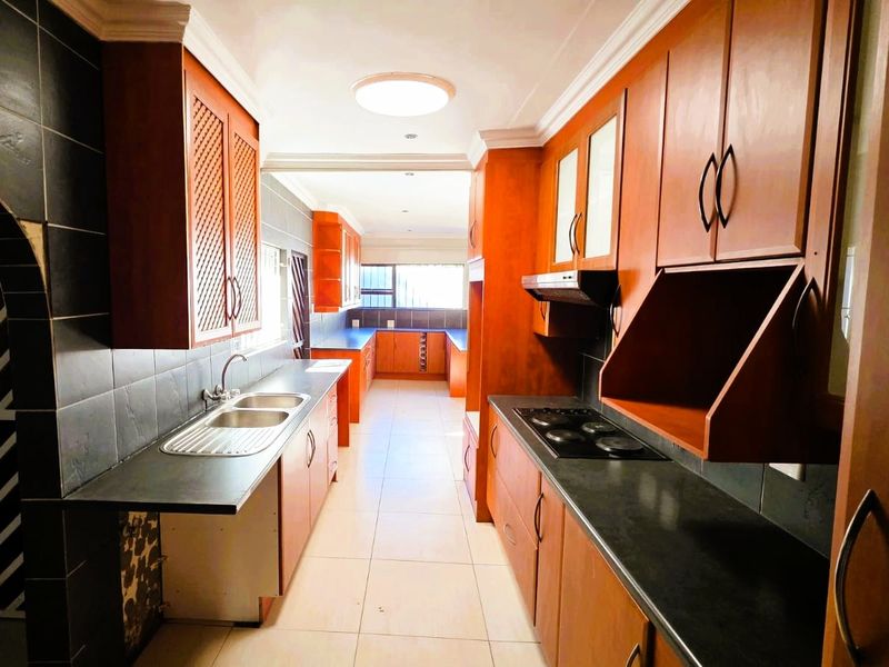 A spacious galley-style kitchen featuring extensive wooden cabinetry, dark countertops, a double sink, and an integrated electric hob with an extractor fan.