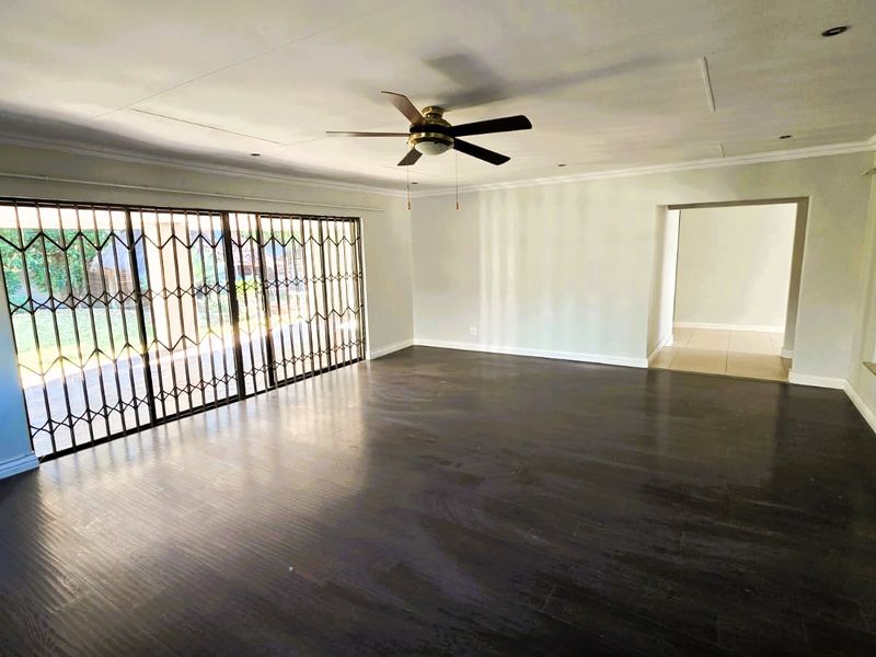 Spacious, empty living room featuring dark laminate flooring, a ceiling fan, and large sliding glass doors with security gates leading to the garden.
