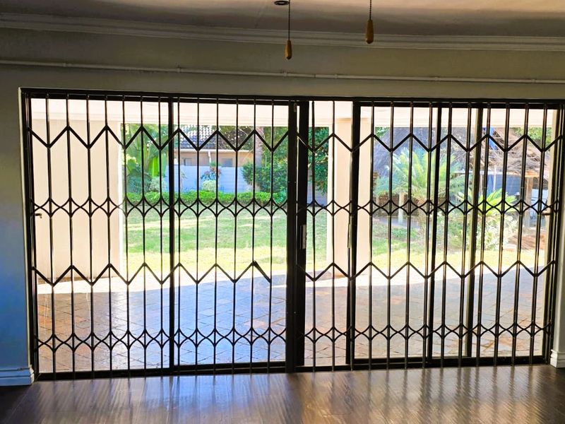 Spacious living area featuring laminate flooring, a ceiling fan, and large sliding glass doors with security gates opening to an outdoor patio.