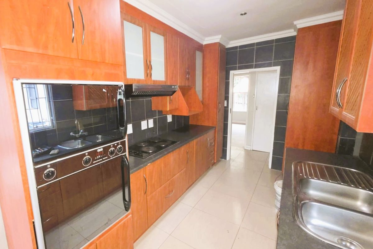 A functional kitchen featuring warm-toned wooden cabinetry, dark tiled backsplashes, integrated appliances, and double stainless steel sinks with ample counter space.