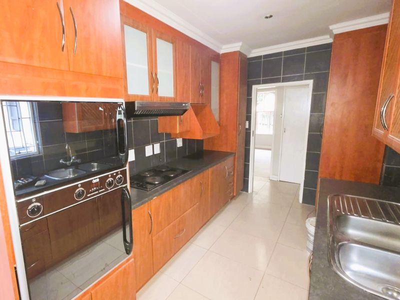 A functional kitchen featuring warm-toned wooden cabinetry, dark tiled backsplashes, integrated appliances, and double stainless steel sinks with ample counter space.