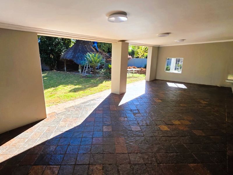 A spacious covered patio featuring durable tiled flooring and structural support columns, offering direct access to the rear garden area.