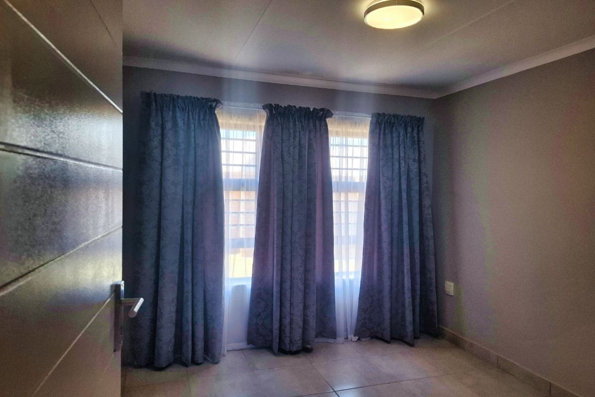 A clean, empty bedroom featuring neutral wall tones, tiled flooring, and large windows dressed with curtains.