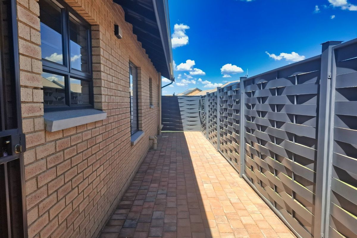 A well-maintained side passage featuring brick exterior walls, paved flooring, and a modern metal privacy screen.