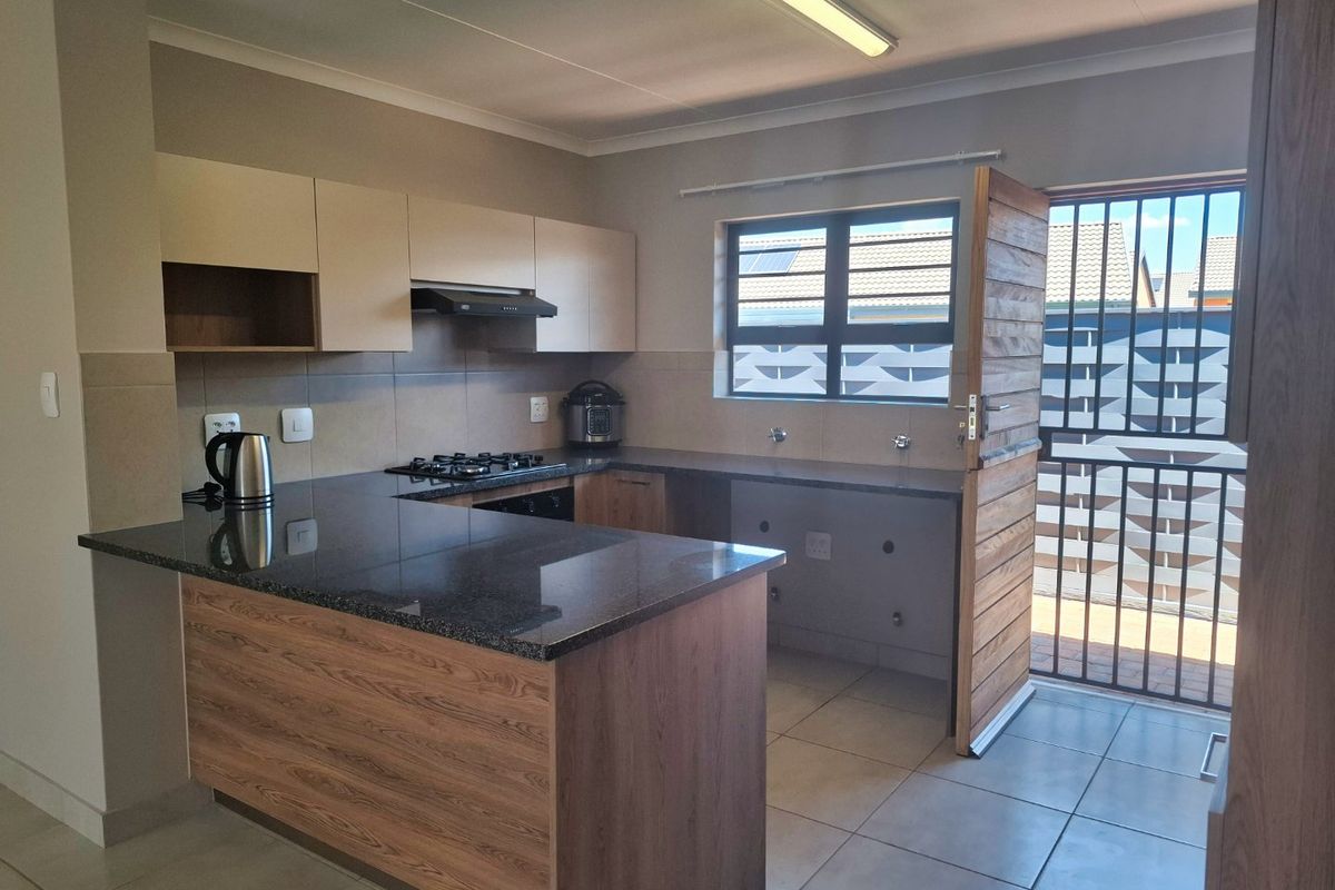 Modern kitchen featuring granite countertops, built-in cabinetry, gas hob, and extractor fan, with direct access to an outdoor area through a security gate.
