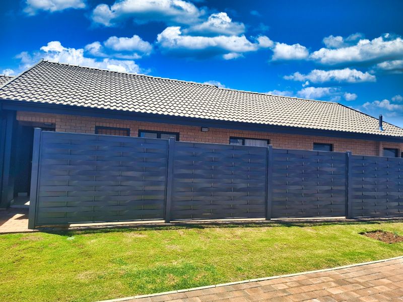 Front exterior view of a brick house featuring a modern privacy screen fence, tiled roof, and well-maintained lawn and paved driveway.