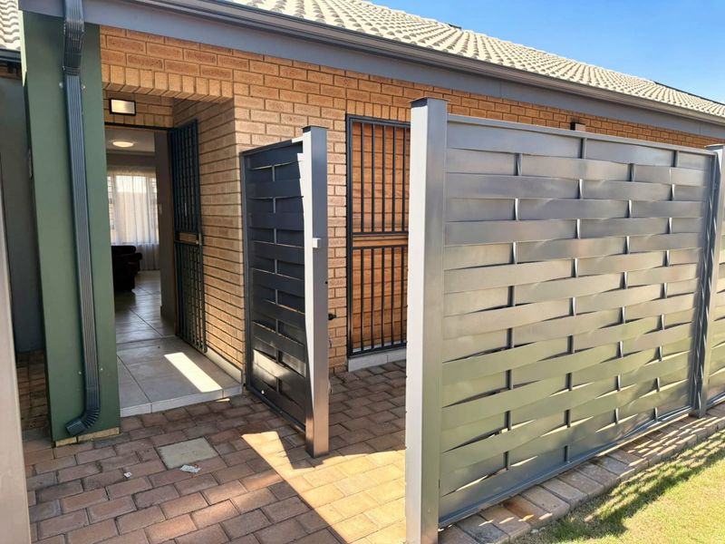 Front entrance area featuring a brick facade, paved walkway, and modern metal privacy screening with a secure gate.