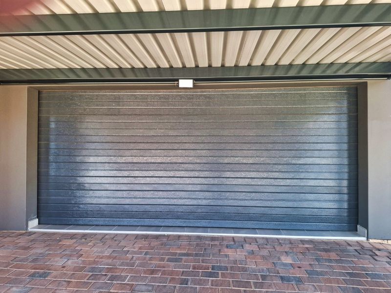 A clean and well-maintained double garage featuring a modern sectional door, corrugated metal roofing, and a paved driveway.