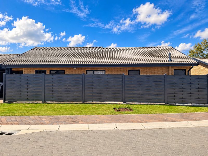 A well-maintained front exterior view featuring a brick facade, tiled roof, and a modern dark privacy fence bordering a neat lawn and paved driveway.