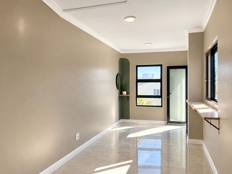 A bright, modern living area featuring polished tile flooring, neutral wall tones, crown molding, and black aluminium framed windows and door.