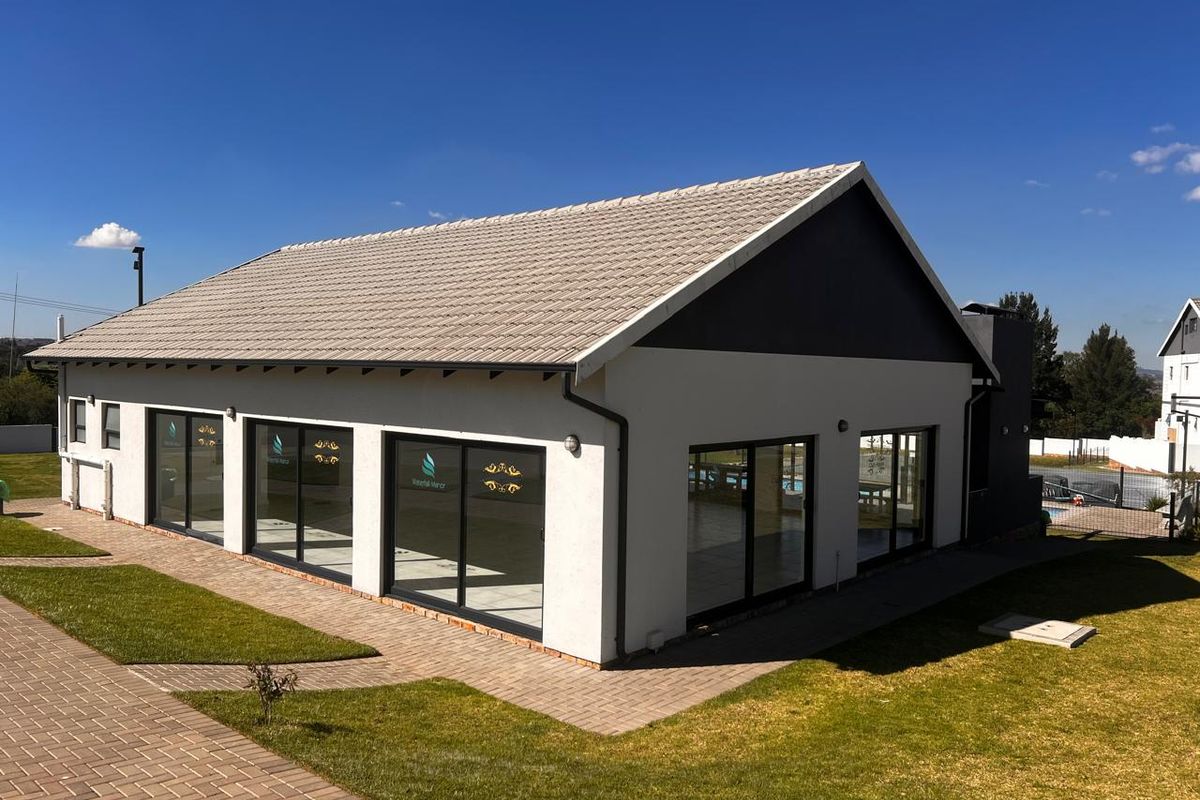 A well-maintained rear exterior view of the property featuring a tiled roof, modern sliding glass doors, and neatly paved walkways set within a landscaped garden.