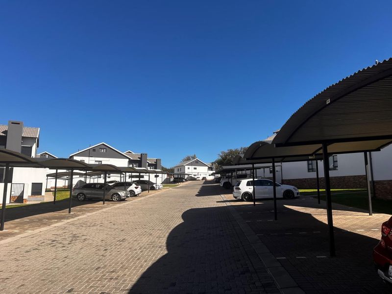 A well-maintained residential complex driveway featuring multiple covered parking bays and paved surfaces under a clear blue sky.