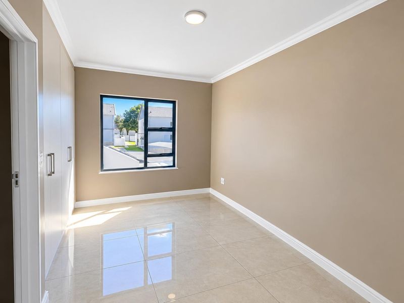 A bright, empty bedroom featuring polished tiled flooring, built-in cupboards, and modern aluminium window frames with neutral wall tones.