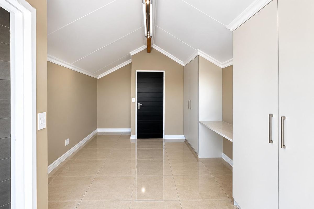 A bright, empty bedroom featuring vaulted ceilings, polished tile flooring, and extensive built-in cabinetry with an integrated desk area.